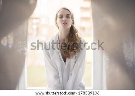 beautiful young woman in white shirt sitting on the window