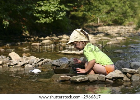 Kid playing with stones and water by the mountain river.