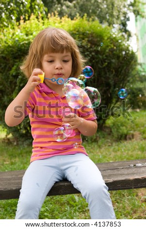 little, cute girl making soap bubbles outdoors