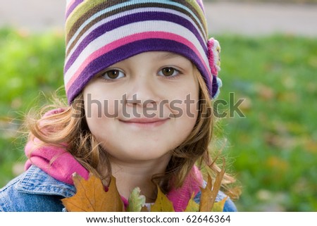 Happy little girl with leaves in Autumn scenery