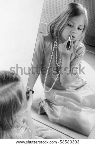 Little girl rouge lips and looking at mirror, studio photo, black and white portrait
