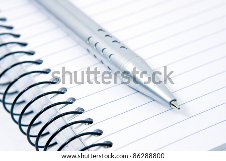 Silver professional business pen next to a blank spiral lined note pad for taking down and writing notes, reports, messages and letters. Perfect notepad for the student, office worker or writer