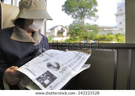 OSAKA, JAPAN-NOVEMBER 6, 2014; lady with mouth mask in Japanese train reading a newspaper. November 6, 2014 Osaka, Japan