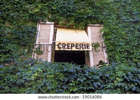 Sign for a French Creperie above a window in a wall grown with ivory