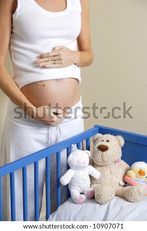 A pregnant woman loves her un-born baby near a crib with stuffed animals