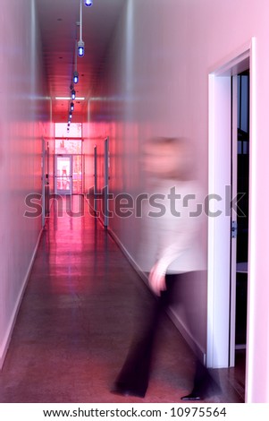 a business woman walks out the door and down the hall of a modern office