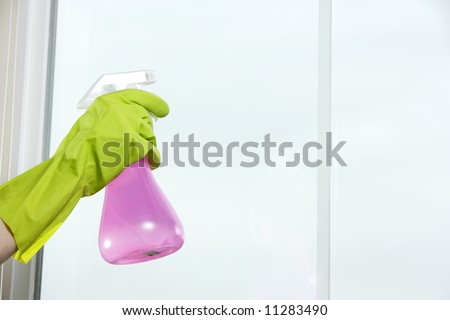 Spraying window cleaner on the glass with a spray bottle and gloves
