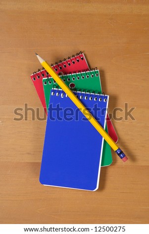 Three note pads sitting on a wooden desk With Pencil