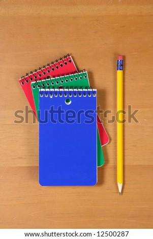 Three note pads sitting on a wooden desk with pencil