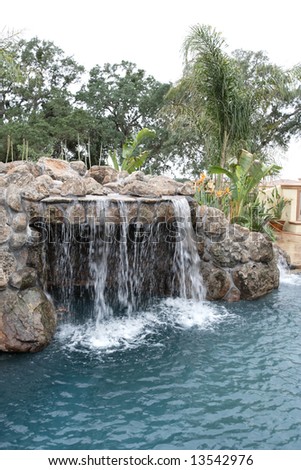 A waterfall in to a pool in a luxury backyard with tropical landscaping