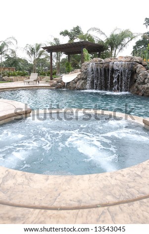 A waterfall in to a pool in a luxury backyard with tropical landscaping