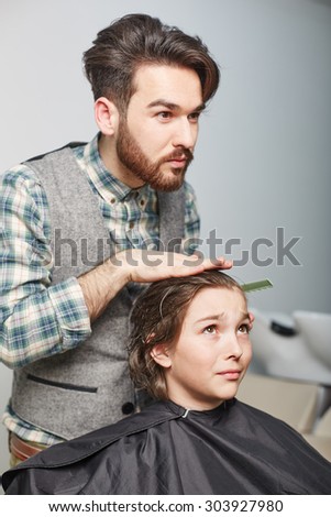 hairdresser cuts hair with scissors on crown of handsome satisfied client in professional hairdressing salon
