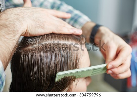 hairdresser cuts hair with scissors on crown of handsome satisfied client in professional hairdressing salon