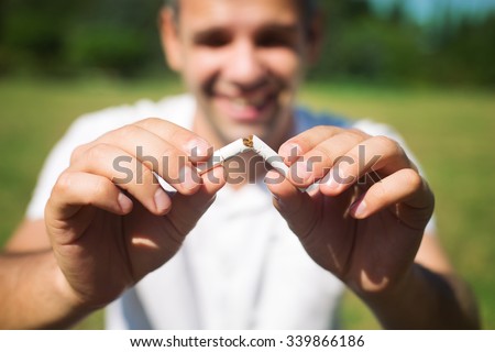 Young man is breaking a cigarette on green background, quit smoking concept