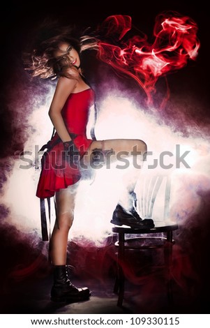 Pretty young woman with flying hair and smoke heart wearing red dress and gun/Danger of love