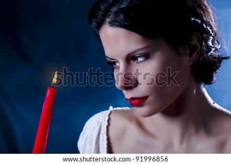 Romantic candle/Beautiful girl, holding the red candle and looking at it. blue background