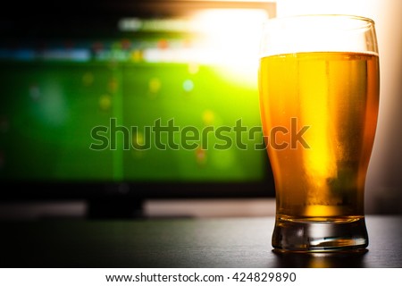 Pint of beer on the table in front of television show off football.