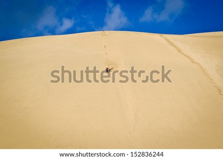 Woman sand boarding on sand dune in New Zealand