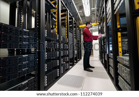 Young IT administrator installing a new rack mount server. Large scale storage server is also seen.