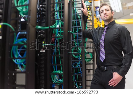 A confident data center manager posing in front of the data center equipment racks.