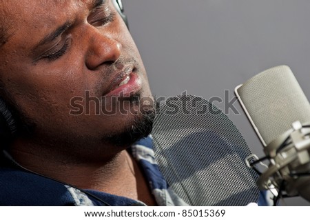 Male singer wearing headphones and singing into a studio condenser microphone equipped with a pop filter