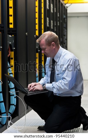 Network administrator is setting up network switches, firewalls and routers using a laptop.