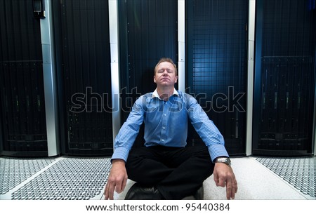 Man sitting in a relaxed meditation posture in front of computer/network data center equipment