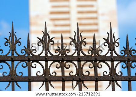 Rusty Wrought Iron Fence / Old and rusty wrought iron fence on blue sky and blurry architecture