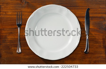 Empty Plate on Wooden Table with Cutlery / Empty and white plate on dark brown table with silver cutlery, fork and knife