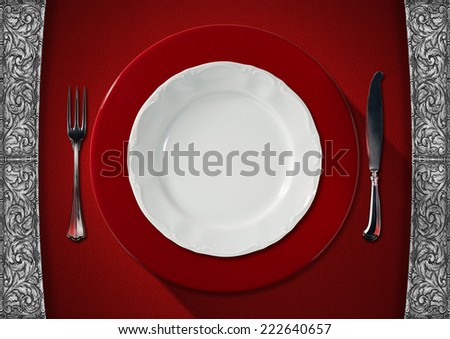 Empty Plate on Red Velvet Background / Empty and white plate on red under plate with silver cutlery, fork and knife on red velvet background with silver floral decorations