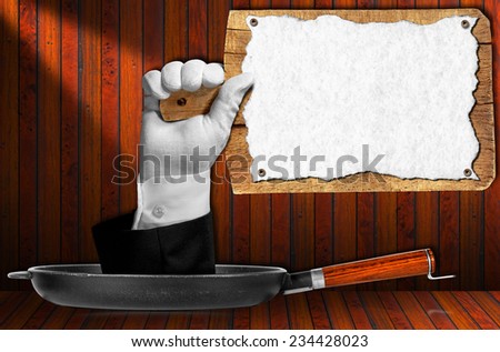 Hand of waiter with white glove come out from a pan with handle and holding an old wooden cutting board with empty sheet of white paper on wooden background