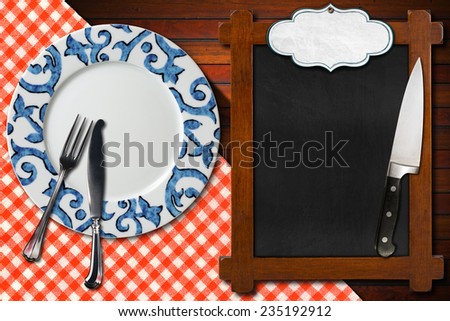 Empty Blackboard Plate and Cutlery / Empty plate with silver cutlery and kitchen knife, empty blackboard for recipes or menu with label on wooden table with red and white checkered tablecloth