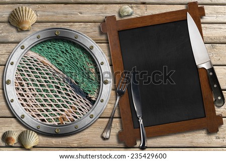 Seafood - Menu Template / Metal porthole with fishing net, empty blackboard, silver cutlery, kitchen knife and seashells on wooden background with sand. Template for recipes or seafood menu