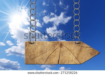 Wooden Directional Sign - One Arrow with Chain. Wooden directional sign with one empty arrow hanging with metal chain on blue sky with clouds and sun rays