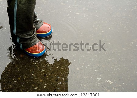 Child standing in wet pants and galoshes in puddle