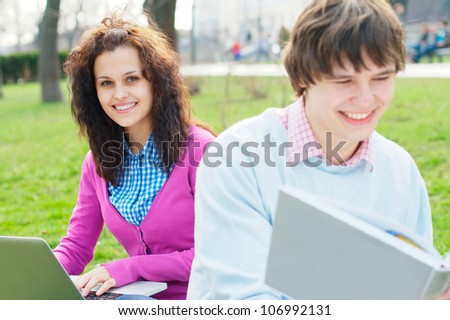 Smiling girl with a laptop with a student at the foreground at the park
