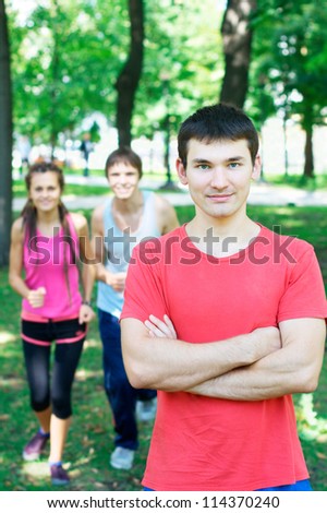 Smiling young man with two people jogging at the background at the park