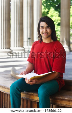 Smiling indian student sitting outdoors with columns at the background