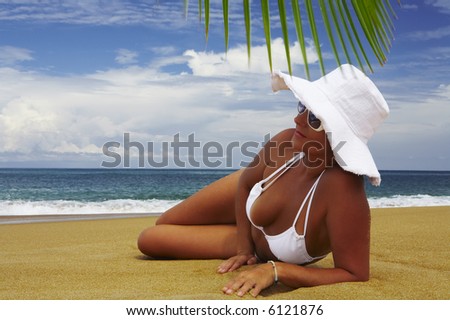 view of nice woman lounging on tropical beach in white panama and bikini