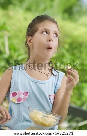 portrait of nice little girl eating chips  in summer environment