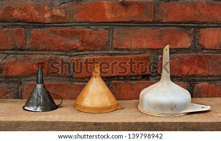 three old fashioned funnels from metal and plastic on rustic wooden surface