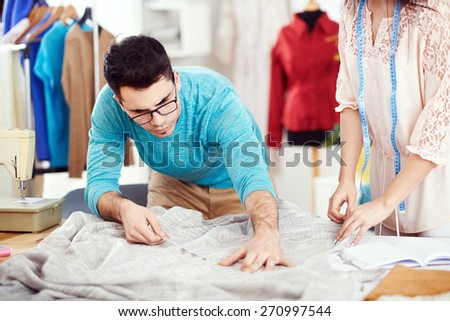 Two young tailors measure material