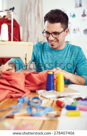 Young male fashion designer working on sewing machine