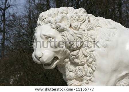 Sculpture of a white lion on a background of the garden trees