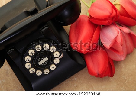 A retro vintage telephone with a bunch of fresh cut red tulips.