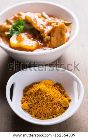 A bowl of curry powder with a Indian curry dish in the background.