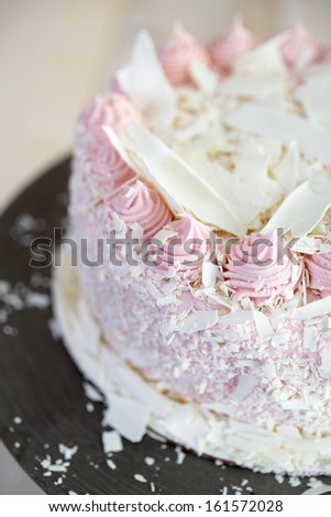 A white chocolate raspberry birthday cake with frosting and shaved white chocolate.