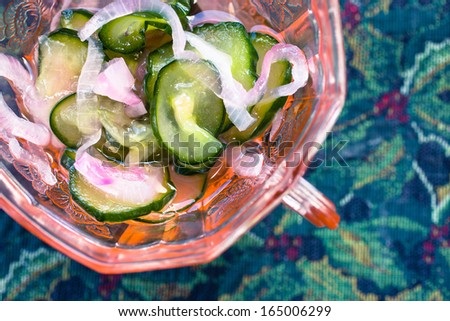A side dish of cucumber pickles in an antique dish with cucumbers and onions.