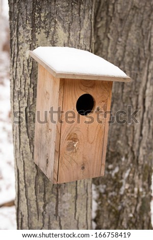 A cedar bird house with snow on the roof in winter.