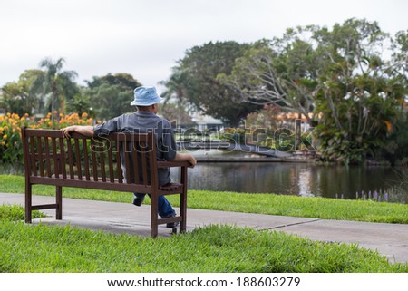 A senior man enjoying a quiet day in the park sitting on a bench.